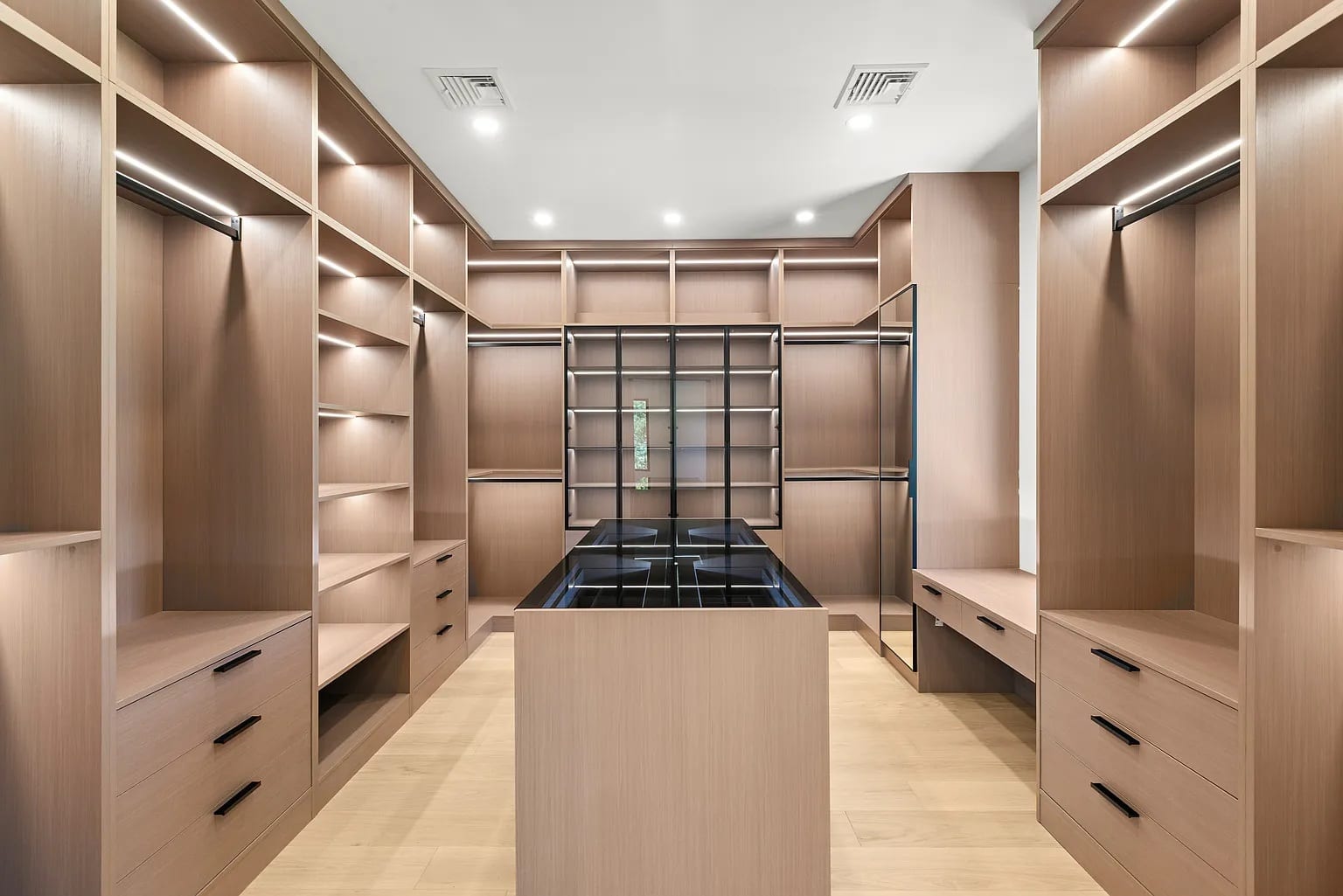 A pale oak dressing room with lit shelving down both walls and a long island between them