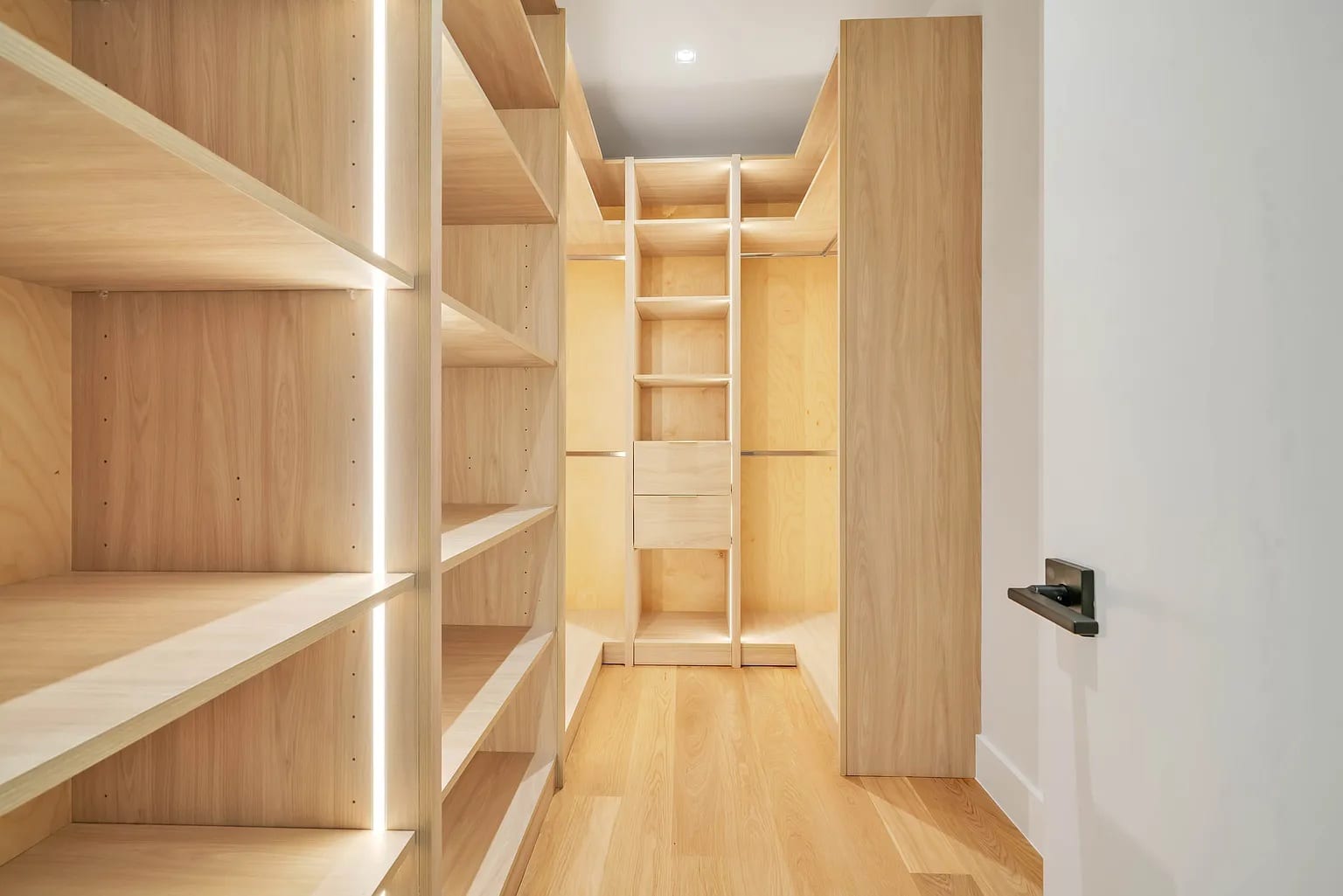 A pale oak walk-in with lit shelving running down the length of the room
